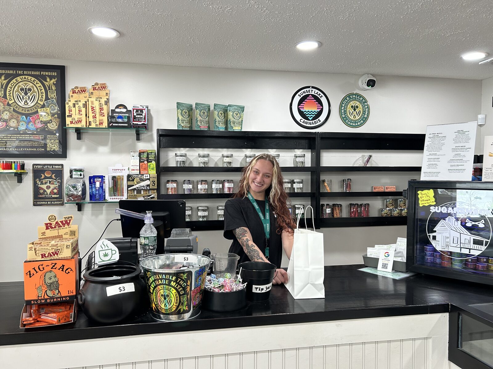 A team member smiling behind the counter at Ideal Cannabis with a filled shopping bag ready for a customer